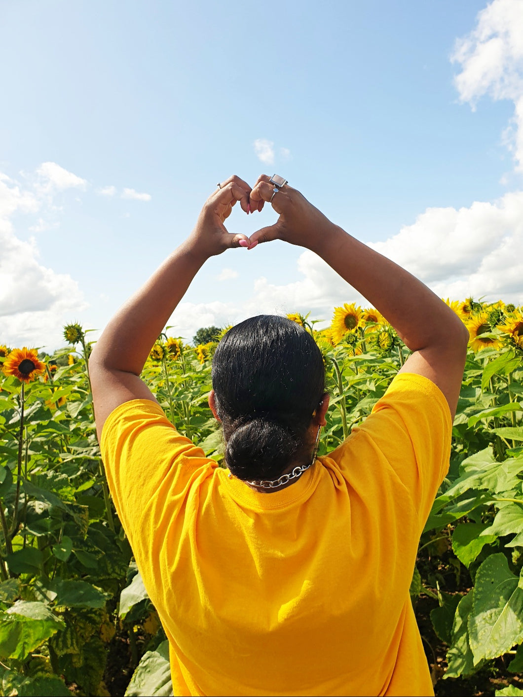 Model making heart shape towards the sky in a sunflower field. Supporting the fact that Pink Runway is about sustainability.