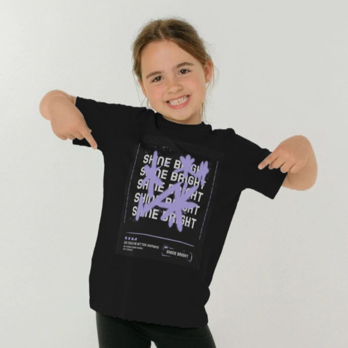 Girl wearing a black T shirt with Graffiti style stars in purple and white text saying Shine Bright beneath. Pink Runway design girls t shirt.